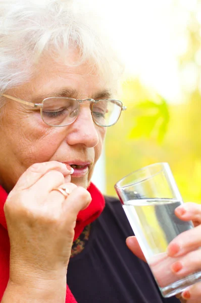 Mujer mayor sosteniendo una píldora en su mano — Foto de Stock