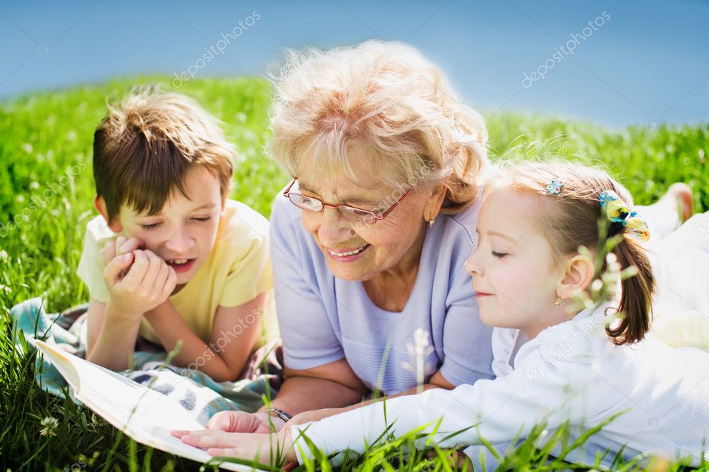 grandmother reading book to grandchildren outdoors