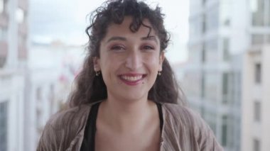 Güzel görünümlü, çok ırklı esmer güzel, zarif, yavaş çekimde kameraya bakıp gülen genç bir kadının yakın plan portresi. Günlük hayat, güzellik. Kadın portreleri. 4k görüntü.