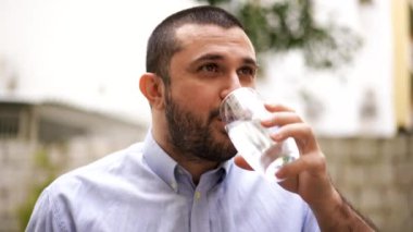 Susamış gülümseyen genç adam dışarıda tek başına ayakta duruyor. Yeni güne sağlıklı bir yaşam alışkanlığıyla başlıyor. Elinde bardakla temiz mineral suyu içiyor. Yaşam tarzı sağlık hizmeti kavramı