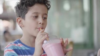 Şirin Çocuk Kafe 'de Pipette' le milkshake içiyor. Slow Motion Little Child çilekli süt içiyor. Sağlıklı yaşam tarzı Çocuklar.
