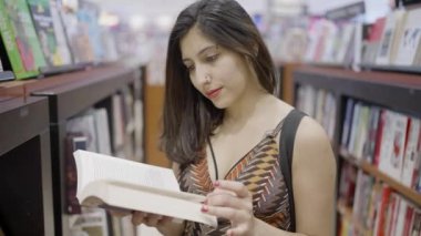 Genç çekici bir kadın alışveriş merkezindeki bir kitapçıda bir kitabı eleştiriyor. Ağır çekim. Kitap okuyan genç bir kız çok mutlu görünüyor. Kişisel gelişim, kütüphane kavramı.