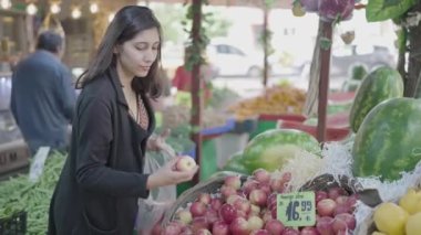 Young attractive woman shopping at the greengrocer choosing apple. She consumes fresh organic fruits for a healthy life. City life concept. Vegan food ingredients. Buy fruit and vegetables.