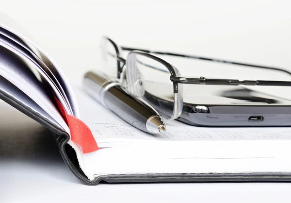 Telefon, Stift und Brille auf dem Notizbuch — Stockfoto