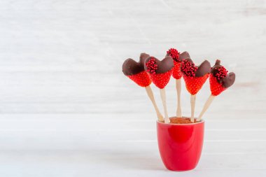 Chocolate covered strawberries in red vase on white wooden background with copy space.