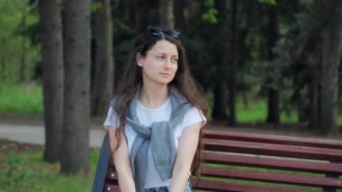 Güzel, genç, esmer kadın sıcak bir yaz gününde düşünceli bir şekilde bankta oturur.