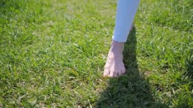Yazın çimenlerde çıplak ayakla yürüyen bir kadının çıplak resmi.