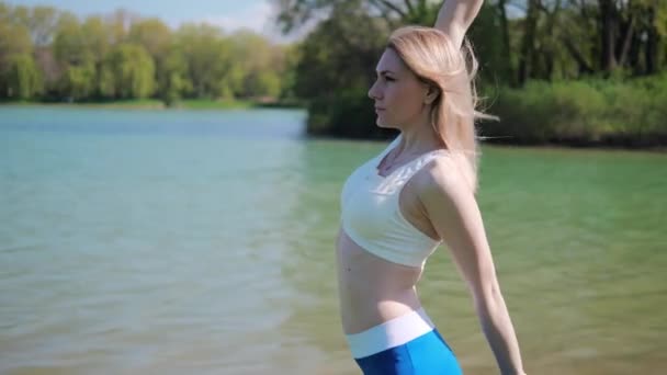Jeune femme sportive faisant des exercices d'étirement dans le parc par une journée ensoleillée. — Video