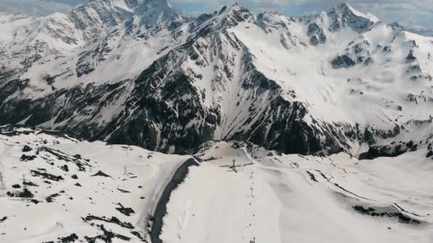 Vuelo aéreo sobre un largo telesilla a una enorme montaña cubierta de nieve. Muchos funiculares escalan el pico nevado de una alta montaña — Vídeos de Stock