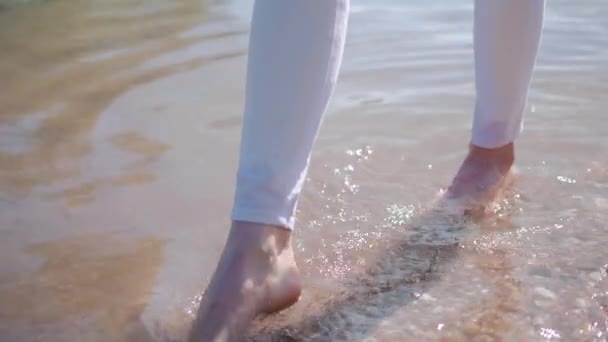 Close-up of barefoot legs in white jeans walking on water — ストック動画