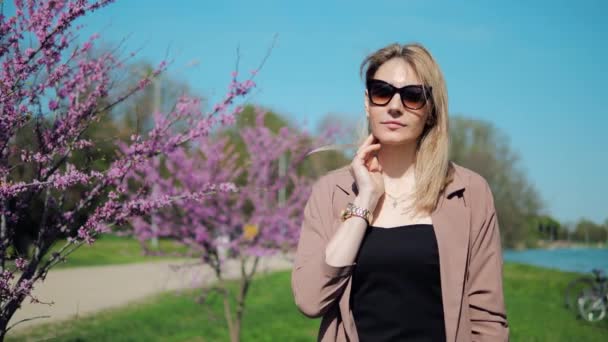 Beautiful woman walks through park and enjoys sights of pink sakura blossoms in spring — Wideo stockowe