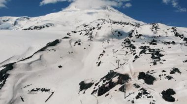 Karla kaplı bir pistte hava uçuşu ve Elbrus Dağı 'na turist ve kayakçıları götüren füniküllü bir teleferik.