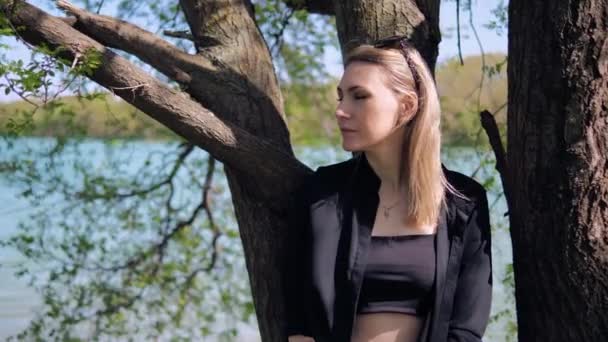 Une femme blonde est debout près d'un arbre et attend quelqu'un — Video