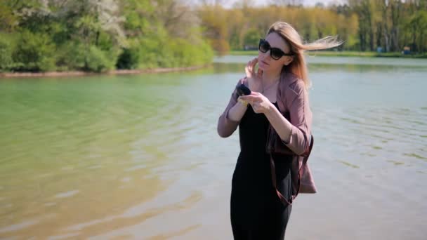 Young beautiful woman corrects her hairstyle looking in a mirror against the background of beautiful nature — Stock Video