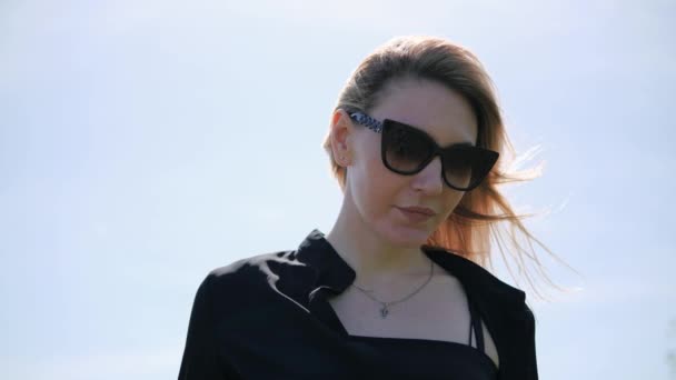 Portrait of a young blonde woman in black sunglasses on the background of a bright sunny sky — Stock videók