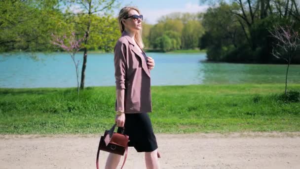 Mulher de negócios bonita nova com uns passeios através de um parque ao longo do lago em um dia de verão — Vídeo de Stock