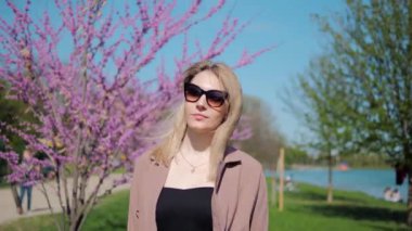 Güzel kız güneşli bir günde, bahar parkında çiçek açan bir sakura 'nın altında yürüyor..