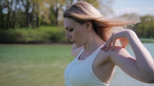 Retrato de mujer joven de cerca haciendo ejercicios de estiramiento manual antes de clases al aire libre en el parque junto al lago. — Vídeo de stock