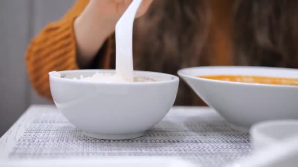 Close-up of a woman in a restaurant at the table takes a spoon and eats rice and Tom Yum soup. Asian dishes. — Stock Video