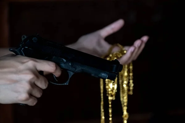 The hands holding gun in the right and necklace gold in the left.