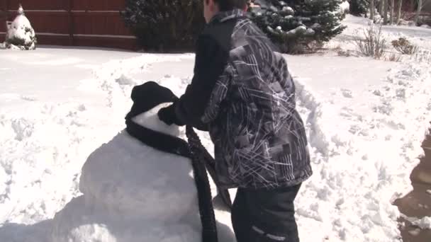 Мальчик кладет лицо на снеговика — стоковое видео