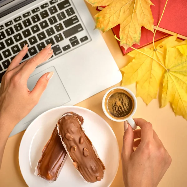 The girl makes a coffee break in the workplace. Profiteroles with cream with a Cup of coffee and a laptop — Stock Photo, Image