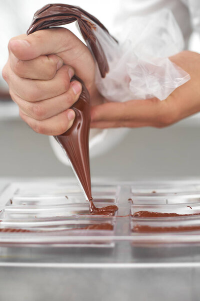 производство, приготовление пищи и концепция людей - кондитер с трубопроводом мешок выдавливания жидкого шоколада в шоколадной форме в кондитерской, закрыть