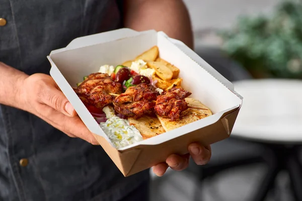 Fast food delivery.Greek souvlaki,salad and gyros take away. menu, serving in recyclable paper container in the hands of the chef.