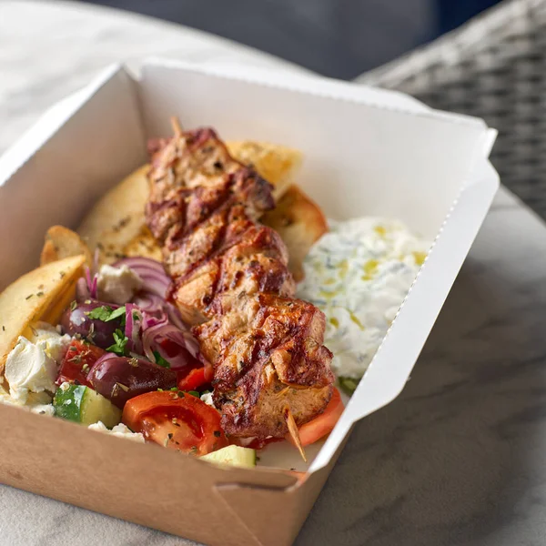 Fast food delivery.Greek souvlaki,salad and gyros take away menu from fastfood restaurant served in recyclable paper plates on table.