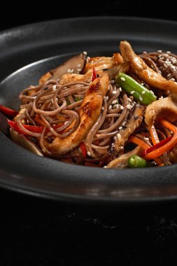 Üst manzara, Soba bifteği ve sebzeler, koyu taştan bir arka planda karabuğday eriştesi. Asya mutfağı, Wok menüsü. Geleneksel Asya yemekleri, Wok menüsü. Yukarıdan dikey üst görünüm