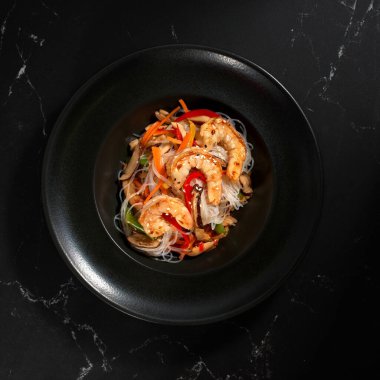 Siyah arka planda karides ve sebzeli Funchoza, kopyalama alanı. Bardak erişte, geleneksel Asya yemeği, kavrulmuş erişte ya da sıcak buharlı siyah bir kasede tava erişte.