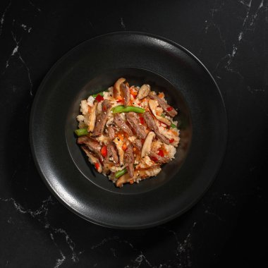 Koyu taştan bir arka planda sığır eti ve sebzeli Çin pirinci. Geleneksel Asya yemekleri, kavrulmuş erişte ya da sıcak buharlı siyah bir kasede rafadan erişte.