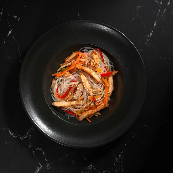 Siyah arka planda tavuk ve sebzeli Funchoza, kopyalama alanı. Bardak erişte, geleneksel Asya yemeği, kavrulmuş erişte ya da sıcak buharlı siyah bir kasede tava erişte.