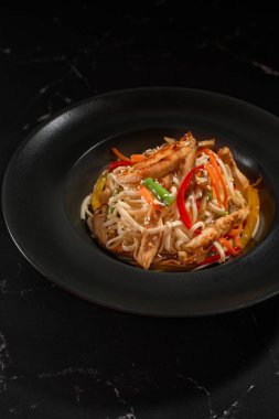 Geleneksel Asya Makarnası. Tavuk ve sebzeli udon erişteleri siyah taş arka planda bir tabakta. Wok menüsü. Yukarıdan dikey üst görünüm
