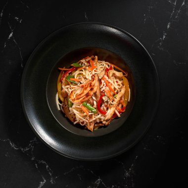 Geleneksel Asya Makarnası. Tavuk ve sebzeli udon erişteleri siyah taş arka planda bir tabakta. Düz konum, Wok menüsü. Üst görünüm