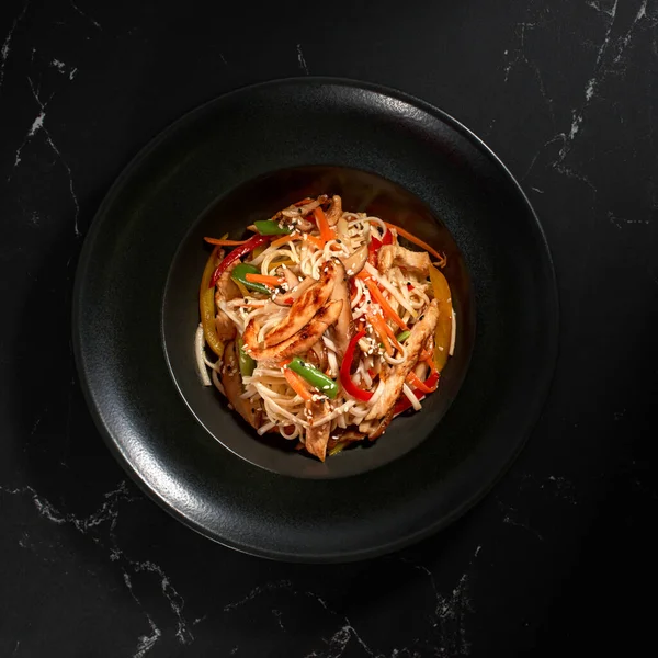 Geleneksel Asya Makarnası. Tavuk ve sebzeli udon erişteleri siyah taş arka planda bir tabakta. Düz konum, Wok menüsü. Üst görünüm