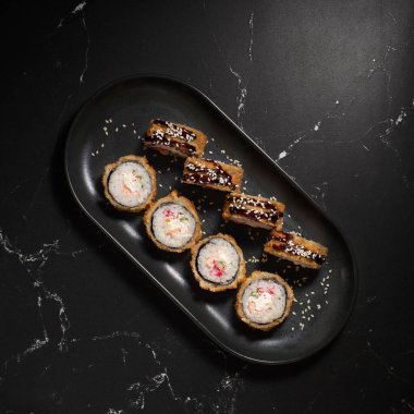 Sıcak kızarmış suşi ruloları ve karides, krem peynir, avokado ve wasabi ile siyah taş üzerinde, seçici odaklanma. Japon mutfağı. Kızarmış. Suşi menüsü. Kapat.