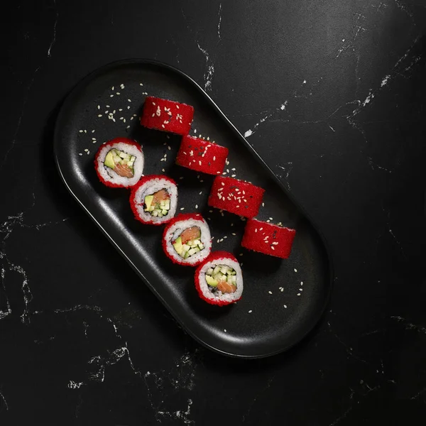 Siyah arka planda geleneksel lezzetli suşi rulosu. Pilavlı suşi, nori, tobiko havyarı, avokado. Suşi menüsü. Japon mutfağı, restoran. Asya yemekleri