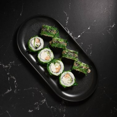 Yeşil suşi. Siyah taşın üzerinde Chuka salatası olan Japon suşisi, seçici odaklı. Japon mutfağı. Suşi menüsü. Asya Diyet Yemeği. Üst görünüm.