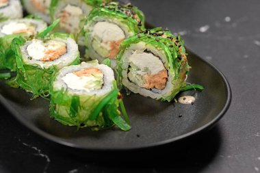 Yeşil suşi. Siyah taşın üzerinde Chuka salatası olan Japon suşisi, seçici odaklı. Japon mutfağı. Suşi menüsü. Asya Diyet Yemeği. Kapat.