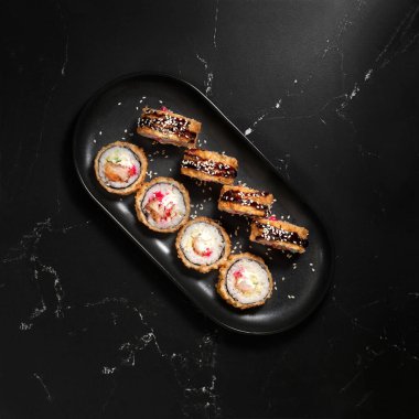 Sıcak kızarmış suşi ruloları ve yengeç, krem peynir, avokado ve wasabi ile siyah taş üzerinde, seçici odaklanma. Japon mutfağı