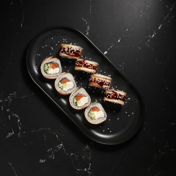 Suşi, Kanada usulü, siyah taşın üzerine yılanbalığı konmuş, seçici odaklı. Japon mutfağı. - Evet. Suşi menüsü.