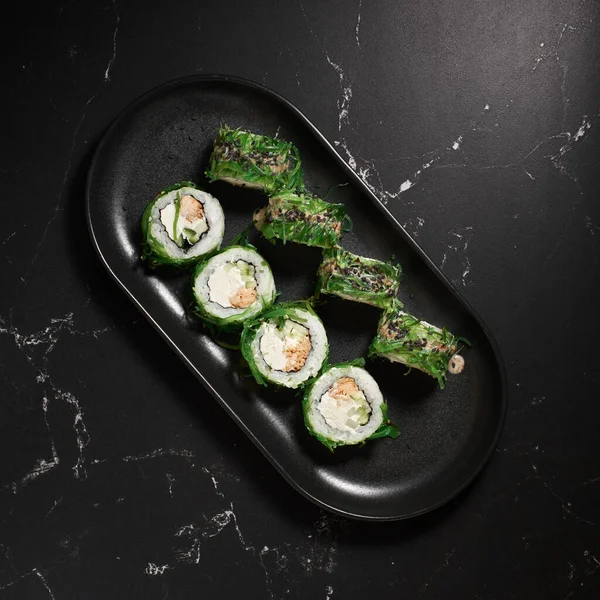 Yeşil suşi. Siyah taşın üzerinde Chuka salatası olan Japon suşisi, seçici odaklı. Japon mutfağı. Suşi menüsü. Asya Diyet Yemeği. Üst görünüm.