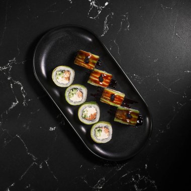 Yeşil Ejder. Siyah desenli arka planda avokadoyla kaplanmış füme yılan balığı unagi ile uramaki suşi rulosu. Suşi menüsü. Japon yemeği. Kapat.