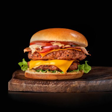 Büyük sandviç, hamburger, sığır eti, domates, salatalık turşusu ve kızarmış pastırma. Ahşap tepside sığır burger, siyah arka planda izole edilmiş..