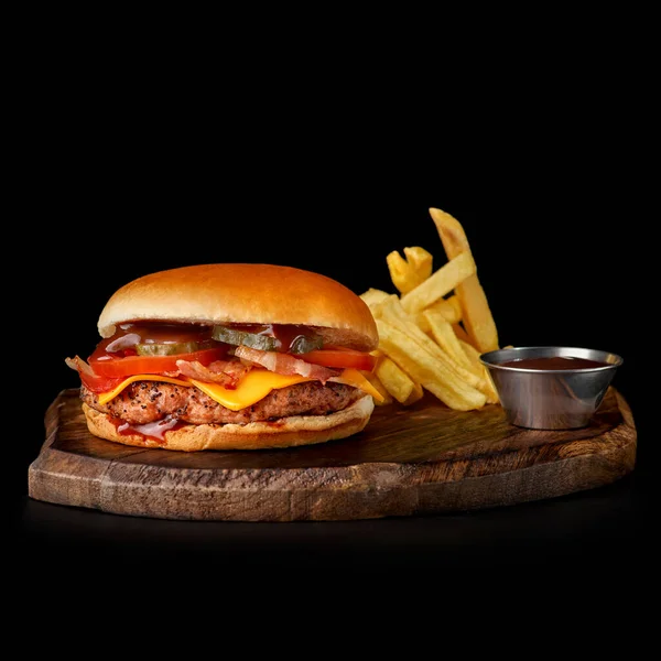 Bacon Burger, Pommes, Tomate auf Holzschneidebrett, isoliert auf dunklem Hintergrund — Stockfoto