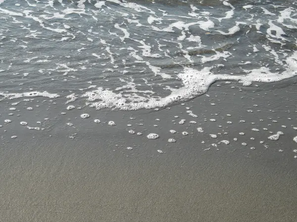 Skummande vatten tvättar i på en Sandy Beach stranden — Stockfoto