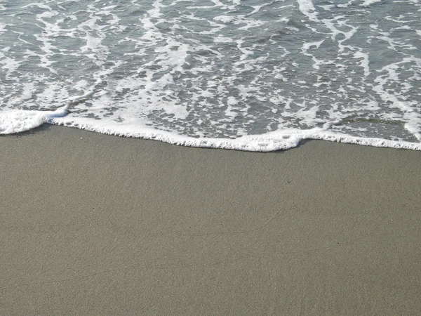 A água espumosa lava-se dentro em uma costa de praia arenosa — Fotografia de Stock