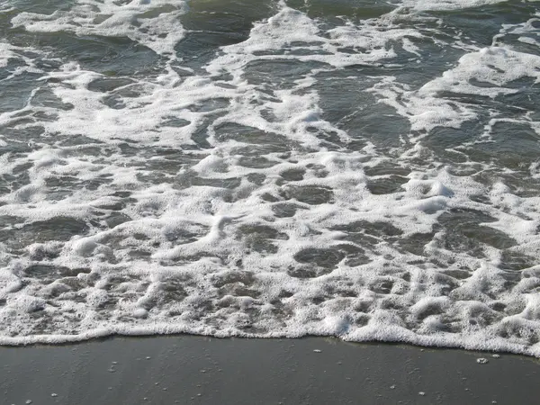 L'eau mousseuse se lave sur une plage de sable fin — Photo