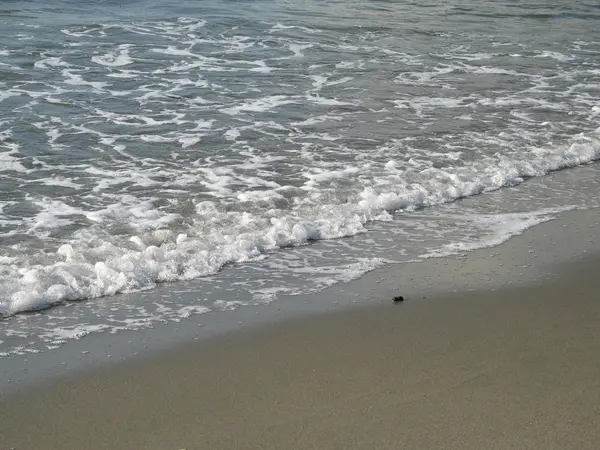 L'eau mousseuse se lave sur une plage de sable fin — Photo